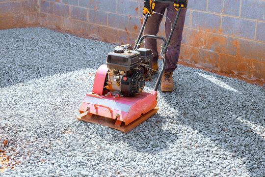 Worker operates vibration plate compactor to flatten gravel at construction site