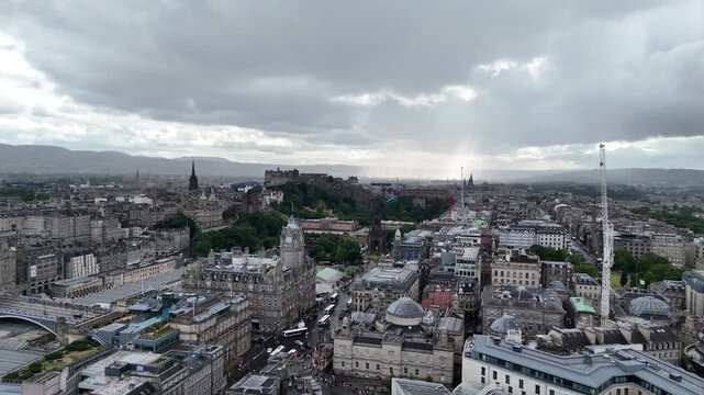 Breathtaking high angle drone view of Edinburgh historic city center featuring the Balmoral Hotel clock tower, Scott Monument, and Edinburgh Castle under dramatic skies, 4k video