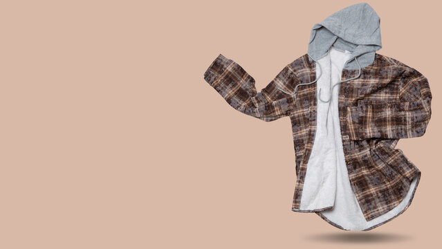 Unbuttoned brown check hooded flannel shirt levitating with copy space on beige background. Open warm fleece lined plaid shacket floating in air