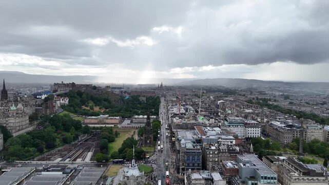Stunning aerial panorama of Princes Street in Edinburgh, showing the Castle, Waverley Station, Scott Monument, Balmoral Clock Tower, and St Andrew Square under dramatic sunbeams, 4k drone footage
