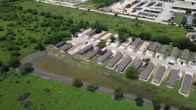 FM 306 access road connects regional commercial hubs with multi unit manufactured housing. High drone view captures retention pond perimeters dividing fields, New Braunfels, Texas
