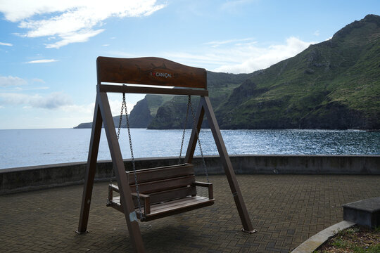 Wooden swing overlooking the Atlantic Ocean and dramatic green mountains in Cani&ccedil;al, Madeira, Portugal, with a peaceful coastal setting and beautiful island scenery.