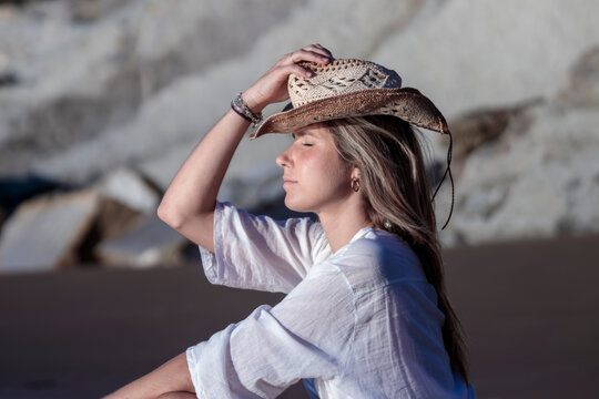 Young woman enjoying sunlight on beach wearing straw hat