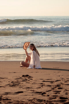 Woman relaxing on beach at sunset holding straw hat