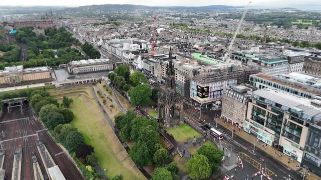Close aerial view of Scott Monument on Princes Street in Edinburgh, showing historic gothic architecture, city traffic, buses, and green park, 4k drone footage