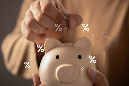 Interest rate growth and savings investment concept featuring a hand depositing a coin into a piggy bank with financial growth, higher returns, saving strategies, and long-term financial planning.