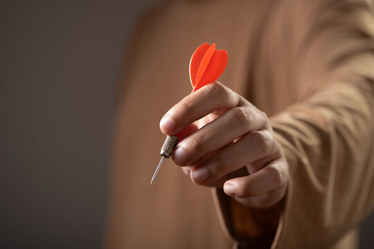 Close-up of a hand holding a red dart, symbolizing goal achievement, target success, focus, precision, business strategy, leadership, determination, planning, and effective decision making.