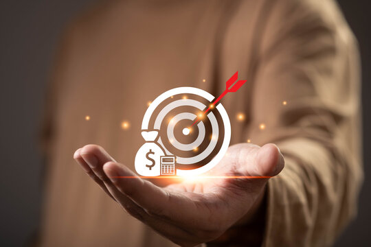 Close-up of an open hand presenting a financial target icon with money bag and calculator, symbolizing financial goals, investment planning, wealth management, budgeting, and business success.