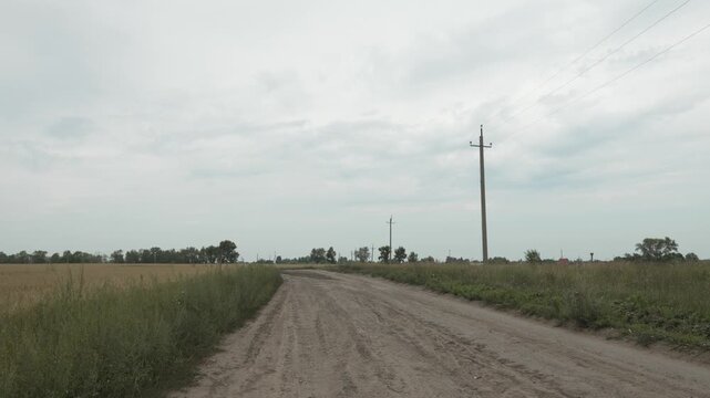 A winding dirt road passes through fields under a cloudy sky.