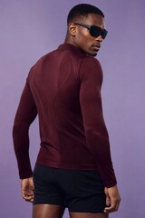 Obraz premium Confident professional man in stylish maroon long-sleeve athletic shirt and dark shorts, side profile with sunglasses, moody purple gradient background, urban streetwear fashion concept