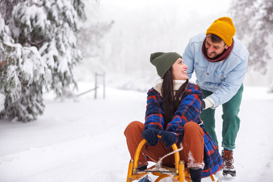 Man pushing woman on sledge while on winter vacation