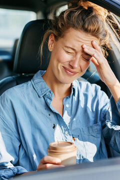 A driver sitting in a modern car, looking down with an amused, face-palm expression at a few drops of spilled coffee on their shirt.