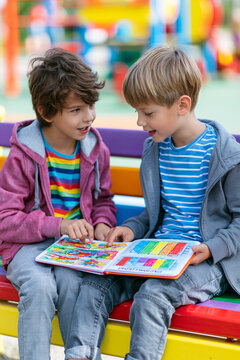 Two kids sitting on a park bench, one of them showing a notebook with colorful drawings and bar charts representing a "business plan.