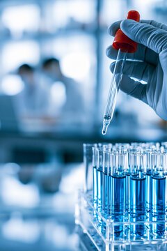 A composite image representing laboratory research, a hand in a white medical glove holds a glass dropper with a red top, near glass test tubes.