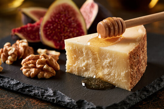 A slate cutting board featuring pecorino or feta cheese, fresh figs cut open, a handful of walnuts, and a  honey dipper.