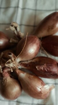 Whole echalion banana shallots with dry, papery peel rests tied together on a white grid-patterned kitchen linen. For cooking shows, culinary blogs, recipe tutorials, organic farming promotions.