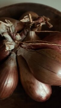 Whole echalion banana shallots with dry, papery peel rests tied together on a white grid-patterned kitchen linen. For cooking shows, culinary blogs, recipe tutorials, organic farming promotions.
