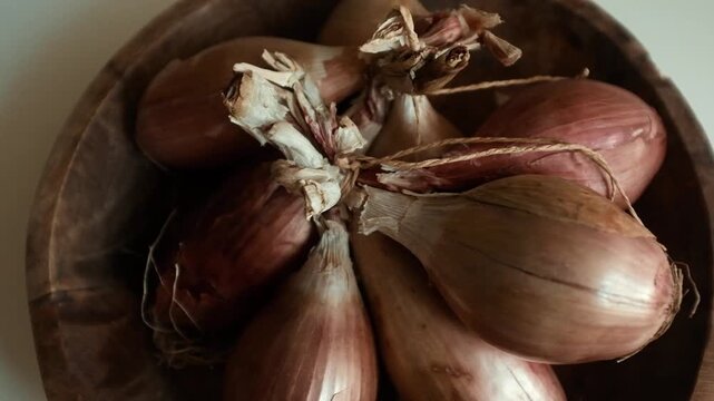 Whole echalion banana shallots with dry, papery peel rests tied together on a white grid-patterned kitchen linen. For cooking shows, culinary blogs, recipe tutorials, organic farming promotions.