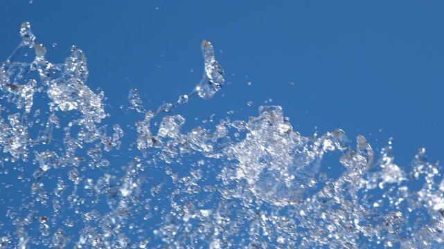 Close-up of sparkling fountain water splashes against clear blue sky. Refreshing droplets create dynamic abstract background representing freshness, summer, energy and motion