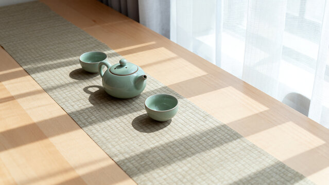 Celadon teapot and two cups on natural linen runner, serene tea time and home decor concept.