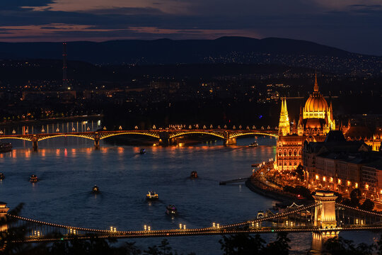 Golden lights illuminate the grand Hungarian Parliament and majestic bridges reflecting on the dark Danube river at night. Such beautiful urban landscapes inspire romantic European travel and tourism.