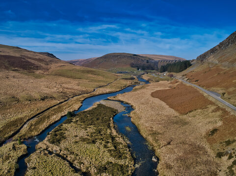 River meanders through rugged, rolling hills under a vibrant blue sky
