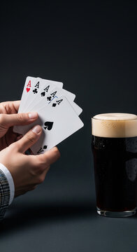 Hand holding four aces playing cards next to a dark beer glass with foam, symbolizing winning, luck, and celebration.