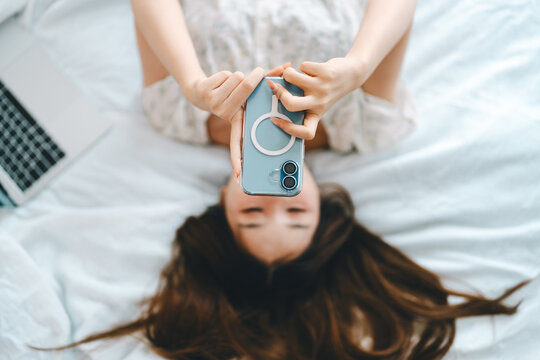 Focus on mobile phone. Woman waking up in bedroom on morning using smartphone internet relax on comfort bed