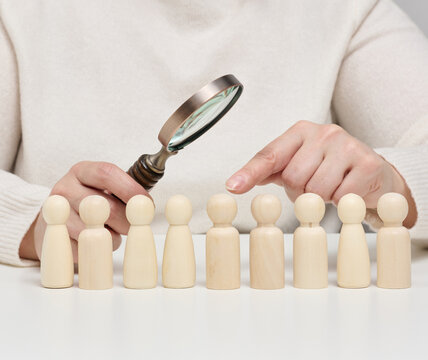 Conceptual photo of the personnel selection and evaluation process with wooden figures of people and a magnifying glass.