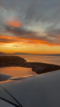 Aerial view from an airplane window during landing over the Croatian coastline at sunrise. The golden morning light illuminates the Adriatic Sea. Vertical video. 