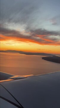 Aerial view from an airplane window during landing over the Croatian coastline at sunrise. The golden morning light illuminates the Adriatic Sea. Vertical video. 
