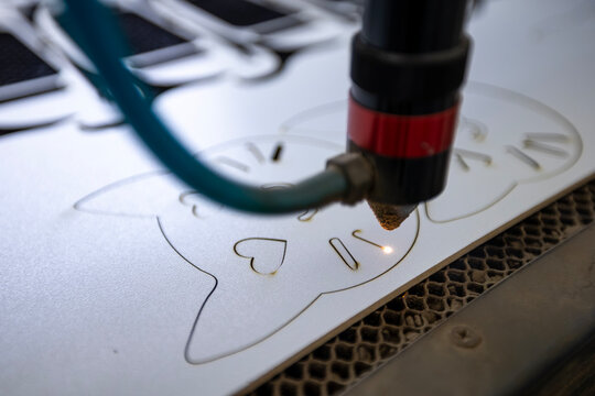 Industrial cnc laser machine carving custom intricate cat designs onto flat white plastic material surfaces within a workshop environment metallic honeycomb base supports and bright focused beams for