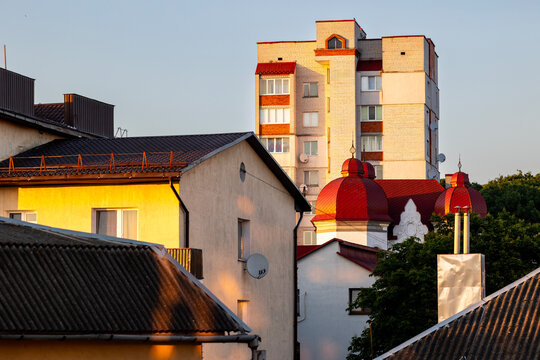 Ternopil, Ukraine urban landscape tall apartment building and domes of Saint Josaphat church at sunset with residential houses, rooflines, lush trees, golden light, and clear blue sky background
