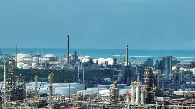 Aerial panorama of coastal energy infrastructure with refineries, processing units, and storage tanks representing global supply chains, fossil fuel dependence, and the pathway toward cleaner energy.
