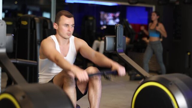 Sportive young man doing exercises on cable rowing device in well-equipped gym . High quality 4k footage