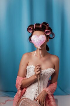 Charming moment of a woman with retro curls playfully hiding her face behind a sparkling heart