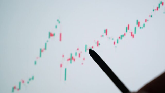 A stock market analyst uses a stylus to examine a digital candlestick chart on a touchscreen, symbolizing technical analysis, trading strategy, market trends, and investment decisions. 4k.
