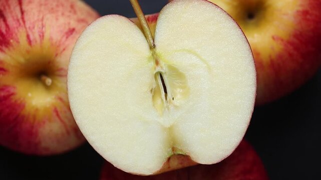 Half of red apple on a rotating pile of apples against a black background. Top view shot