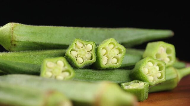Pile of fresh whole and sliced okra rotating on a black background.