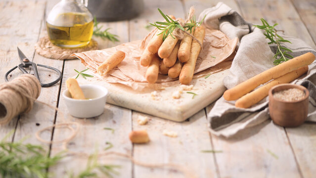 Crispy Italian breadsticks tied with rosemary on a rustic wooden table