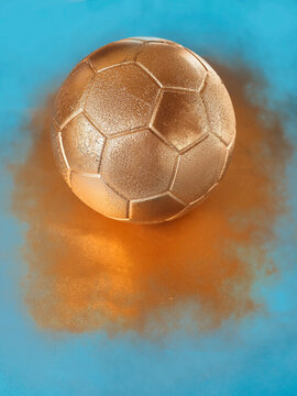 Golden soccer ball surrounded by dust on blue background. Gold highlight high value and profit in this business. Copy space for a message. Abstract football background.