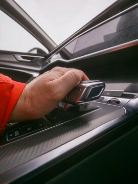 Hand grips car automatic gear box shift. Coffee cup sits beside. Red jacket sleeve visible. Modern luxury car interior shown. Premium high price and value interior vehicle trim.