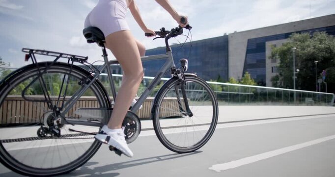 Young beautiful athletic woman in sportswear walking and riding a bicycle in the city in an urban park with a bridge and benches