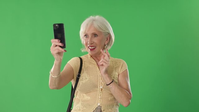 Smiling elderly woman in summer clothes takes selfie on a green background. Chroma key compositing. . High quality 4k footage