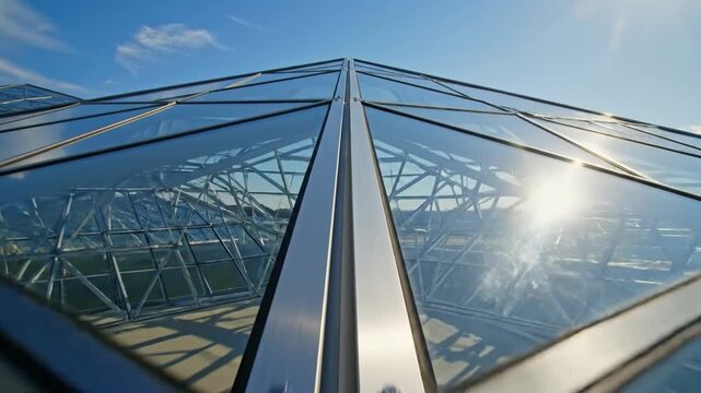 Modern glass pyramid roof with geometric steel frame under a clear blue sky and bright sunlight