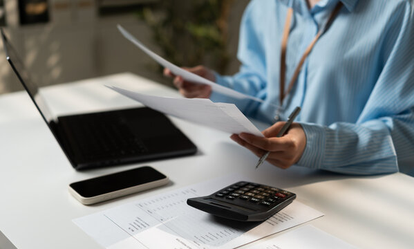 Businesswoman reviewing financial documents with laptop, calculator and paperwork in a modern office, representing accounting, bookkeeping, expense management, tax preparation and corporate finance.