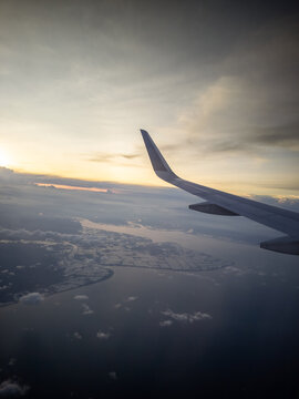 Scenic flight perspective featuring an aircraft wing above the ocean and clouds at golden hour