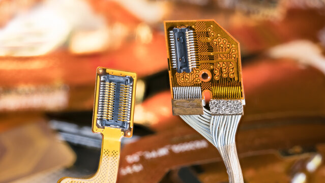 Closeup electronic flex connectors of cellphone, tablet or computer on blur background. Yellow flexible flat cable with contact pins and orange bendy printed circuit board with white electrical wires.