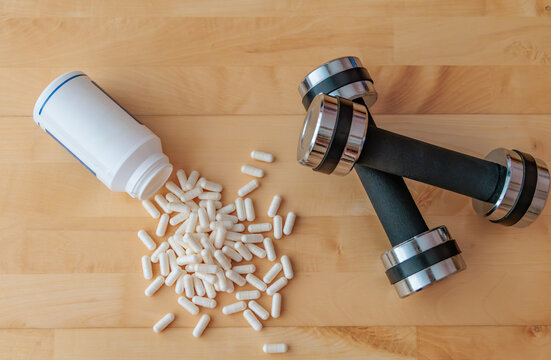 Dietary Supplement Capsules with Dumbbells on Wooden Background for Weight Loss, Fitness and Sports Nutrition