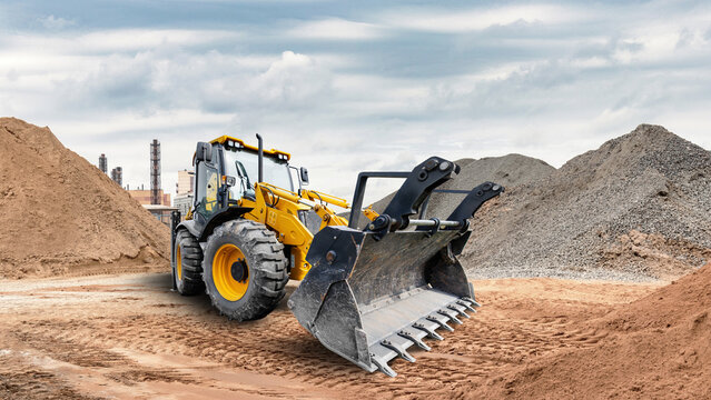 Universal excavator loader is active at a construction site. It is moving dirt and gravel around. The sky is cloudy, and there is construction work taking place